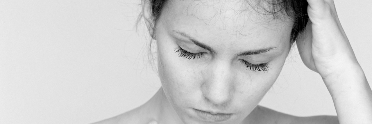 What It's Like to Have Body Dysmorphic Disorder Young woman with bare shoulders in deep reflective thought.