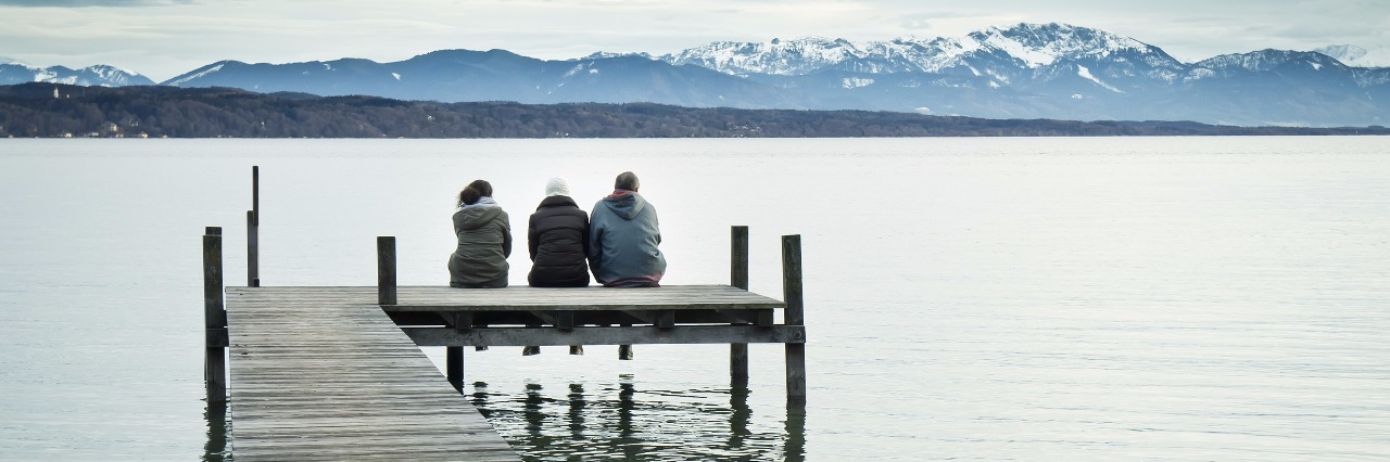 three friends sitting on a dock overlooking a lake and mountains