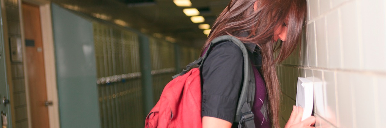 How the Mental Health System Fails Students a student with a backpack leaning on a hall in the hallway
