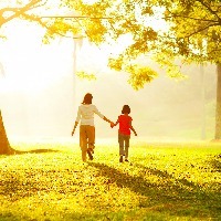 Mother and daughter holding hands, walking through park on sunny day