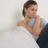 woman sitting on the couch hugging a pillow and thinking