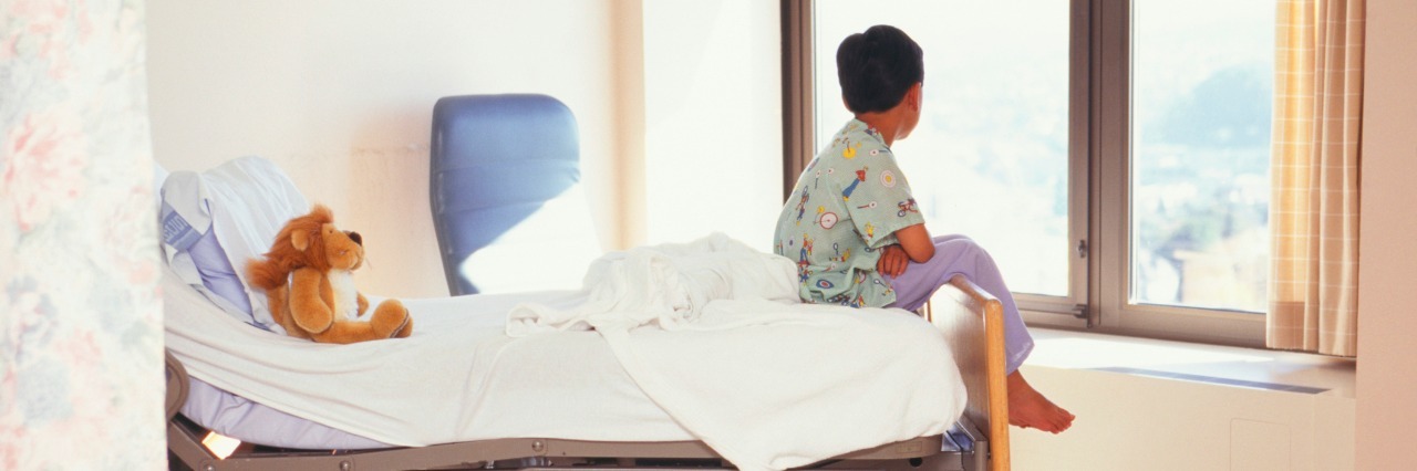 young boy sitting on hospital bed looking out window