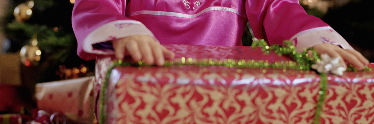 Holiday Lessons for My Son and His Sister With Down Syndrome Girl kneeling by Christmas tree, holding present.