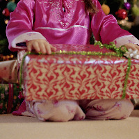 Girl kneeling by Christmas tree, holding present.