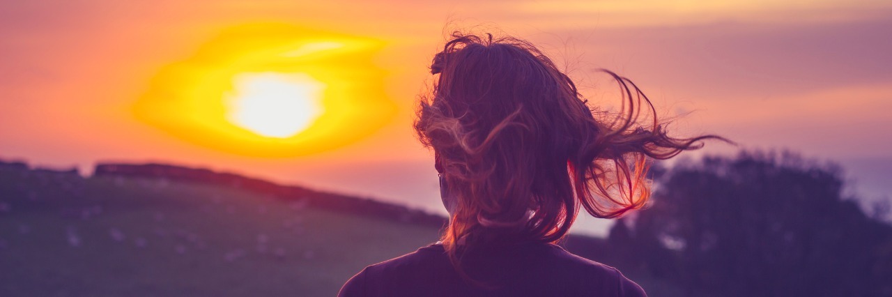 young woman admiring the sunset over fields