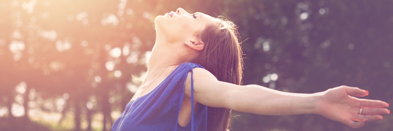 Lyme Disease: Grateful for How My Illness Has Shaped Me woman in blue shirt standing outside next to trees and enjoying the sunshine