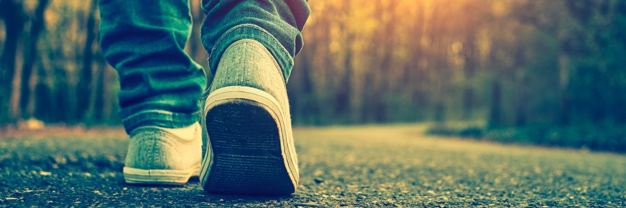 Close-up of person's shoe as they walk on a tree-lined road