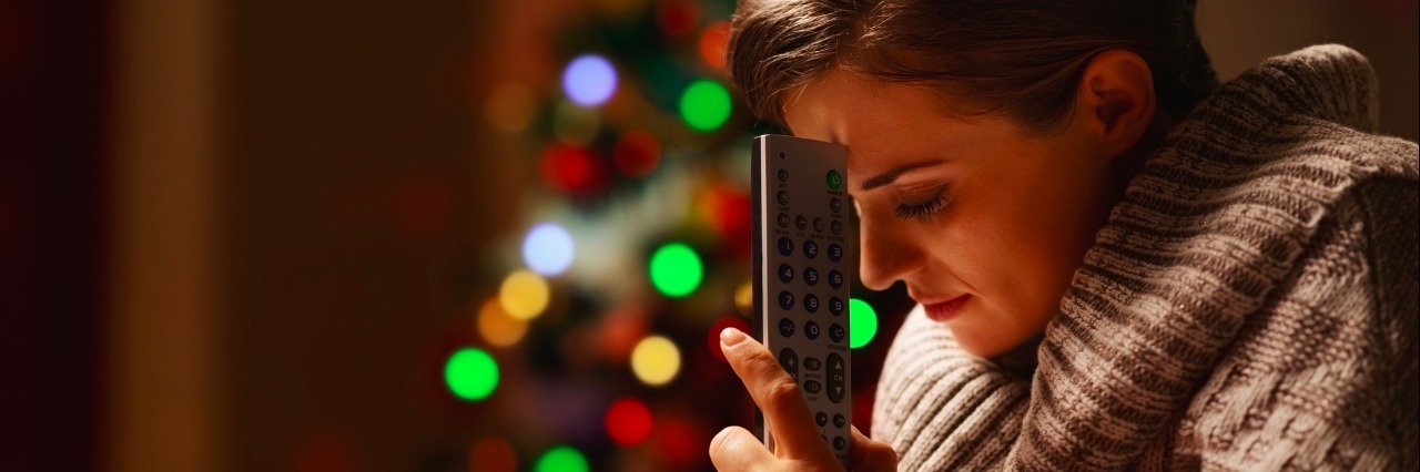 Frustrated woman with tv remote control near christmas tree