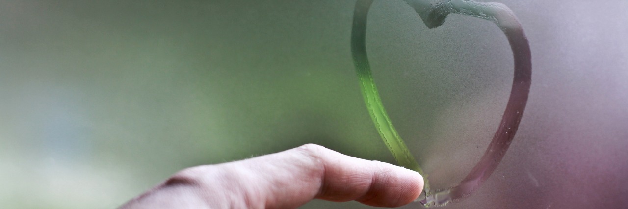 close up on finger drawing heart on frosted glass