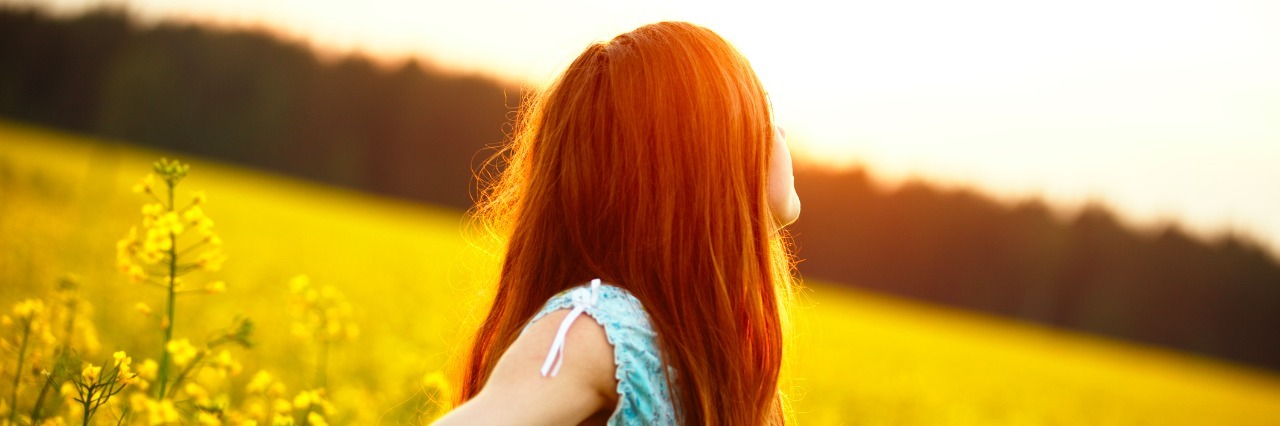 young woman enjoying sunlight with raised arms in canola field