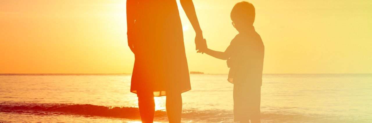 Silhouette of mother and son holding hands and facing the water while standing on the beach