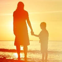 Silhouette of mother and son holding hands and facing the water while standing on the beach