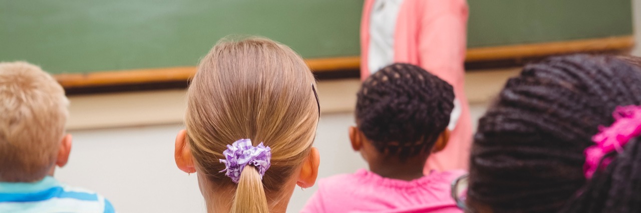 Students sitting at desks as teacher writes on the chalkboard