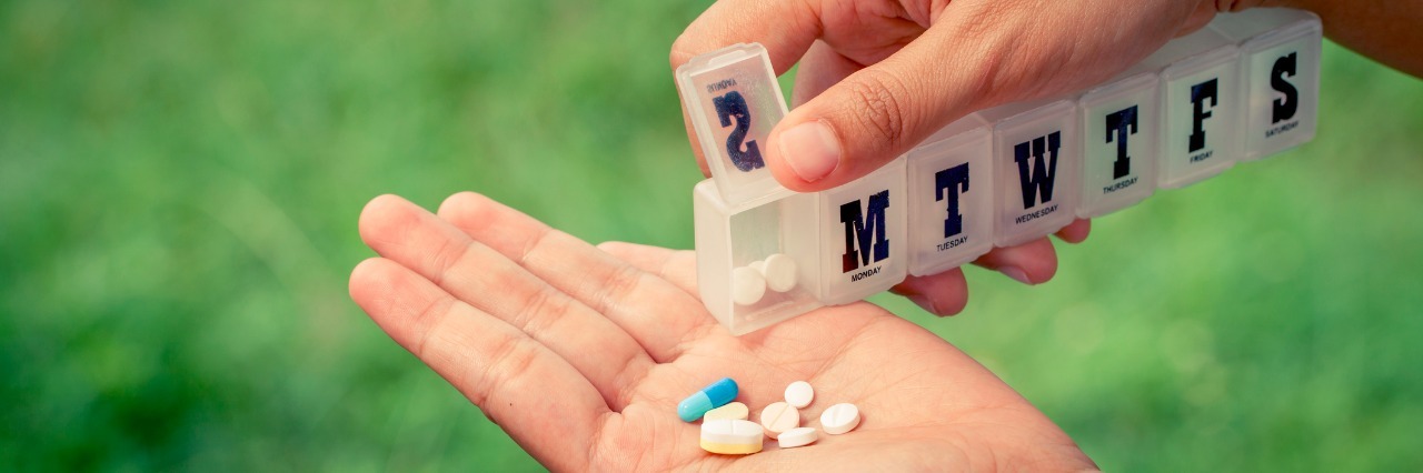 My Love-Hate Relationship With Steroids woman hand pouring pills from a pill reminder box into her hand on green nature background in vintage filter