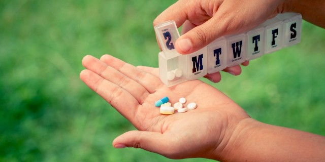 My Love-Hate Relationship With Steroids woman hand pouring pills from a pill reminder box into her hand on green nature background in vintage filter