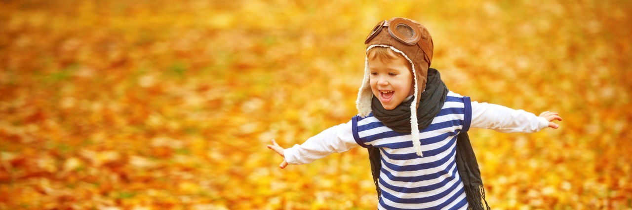 child playing outdoors in pilot outfit among fall leaves