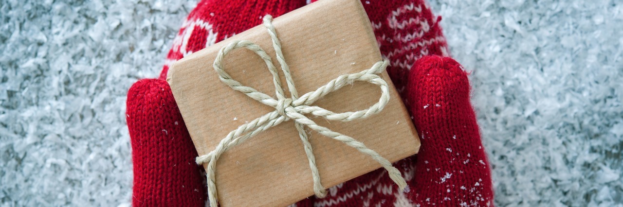 Christmas Gifts for People With Gastroparesis hands wearing festive red and white mittens and holding a small box wrapped in paper and tied with a bow