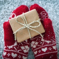 hands wearing festive red and white mittens and holding a small box wrapped in paper and tied with a bow