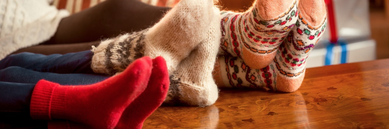 Having Fun When You're Sick at Home During the Holidays three pairs of feet in fuzzy holiday socks resting on a table