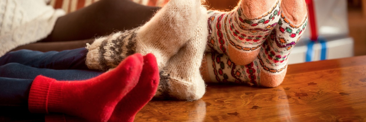 three pairs of feet in fuzzy holiday socks resting on a table