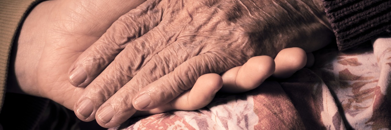Breast Cancer: Lessons About Love From Supporting My Grandmother close up of a young woman holding her grandmothers hand on a hospital bed