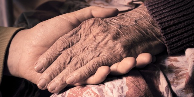 close up of a young woman holding her grandmothers hand on a hospital bed
