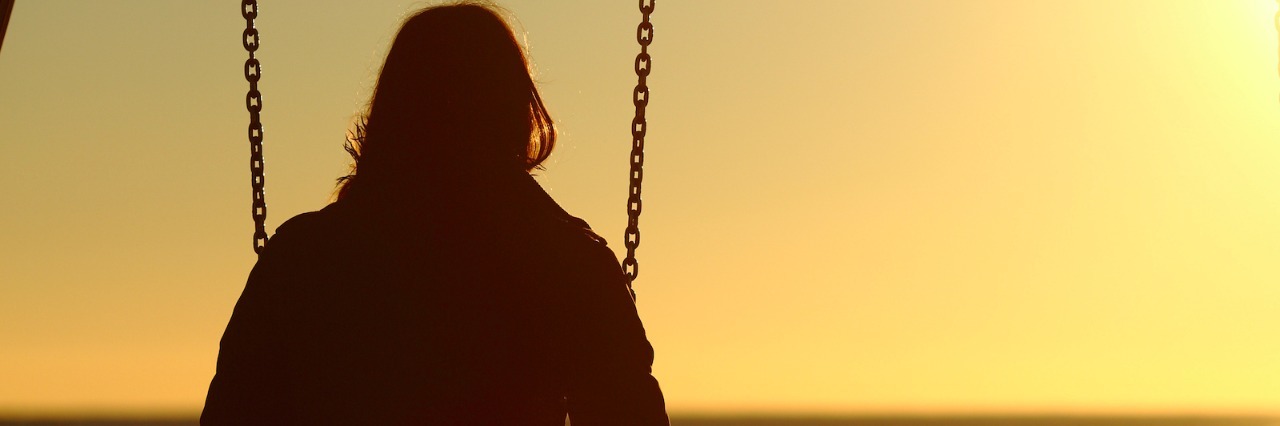 Woman sitting on swing, looking onto the water at sunset