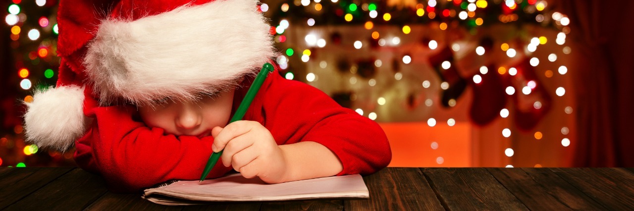 My Son on the Autism Spectrum Won't Have a Picture With Santa, and That's OK boy in santa hat writes a letter to santa with christmas decorations in the background