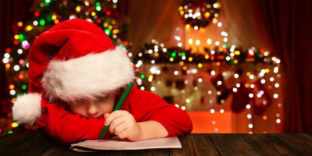 My Son on the Autism Spectrum Won't Have a Picture With Santa, and That's OK boy in santa hat writes a letter to santa with christmas decorations in the background