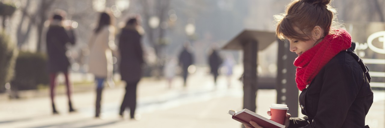 What It's Like Going to Class With Anxiety Girl sitting on a wooden bench, reading a book and drinking coffee, outdoors