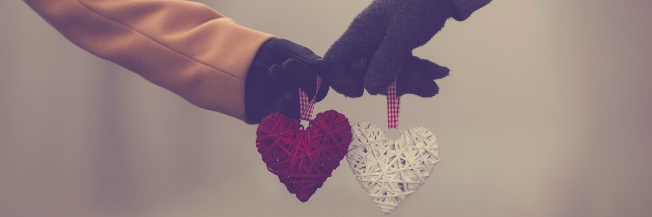 Two people wearing jackets and gloves, holding hearts toward each other