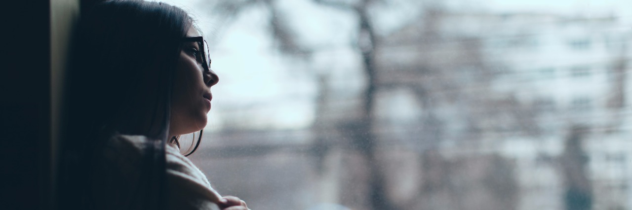 Fearing the Future With Chronic Illness young woman sitting on windowsill and looking out at cold, snowy day