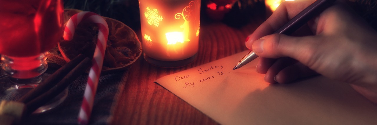 Christmas Wish List for People With Undiagnosed, Chronic Illness a person's hand writing their christmas wish list next to candles and a candy cane