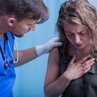 young woman holds her hand over her chest in pain while a male emergency room doctor watches in concern