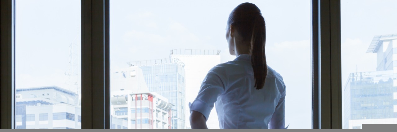 Facing Discrimination in the Workplace Due to Illness, Disability businesswoman stands alone in a conference room and looks out the window