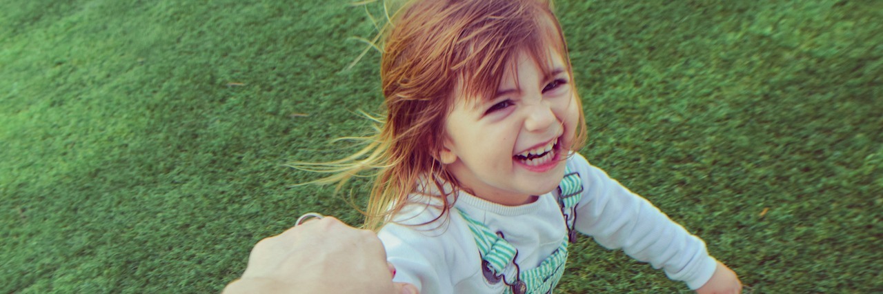 Why I'm Only Having One Child as a Woman With Bipolar Disorder Silly little girl holding a parents hand barefoot in the grass, laughing