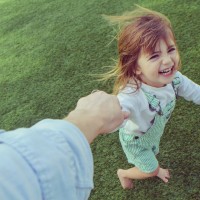 Silly little girl holding a parents hand barefoot in the grass, laughing