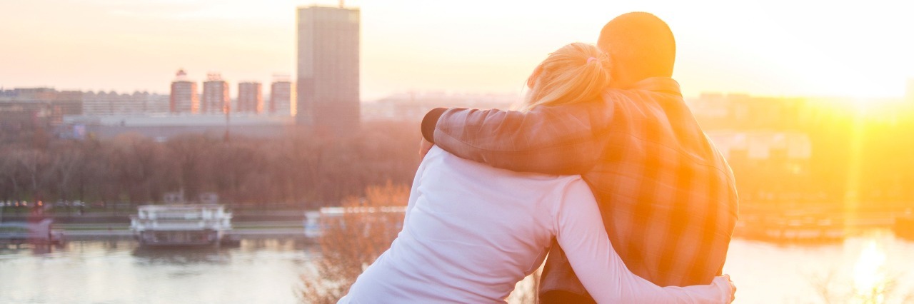 5 Things a Chronically Ill Person Wants Their Friends to Know Rear view of a loving couple sitting on a rampart and looking at river view from above.