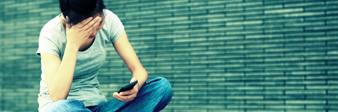 The Supportive Comments That Aren't Helpful for My Chronic Illness woman sitting on ground looking at cell phone