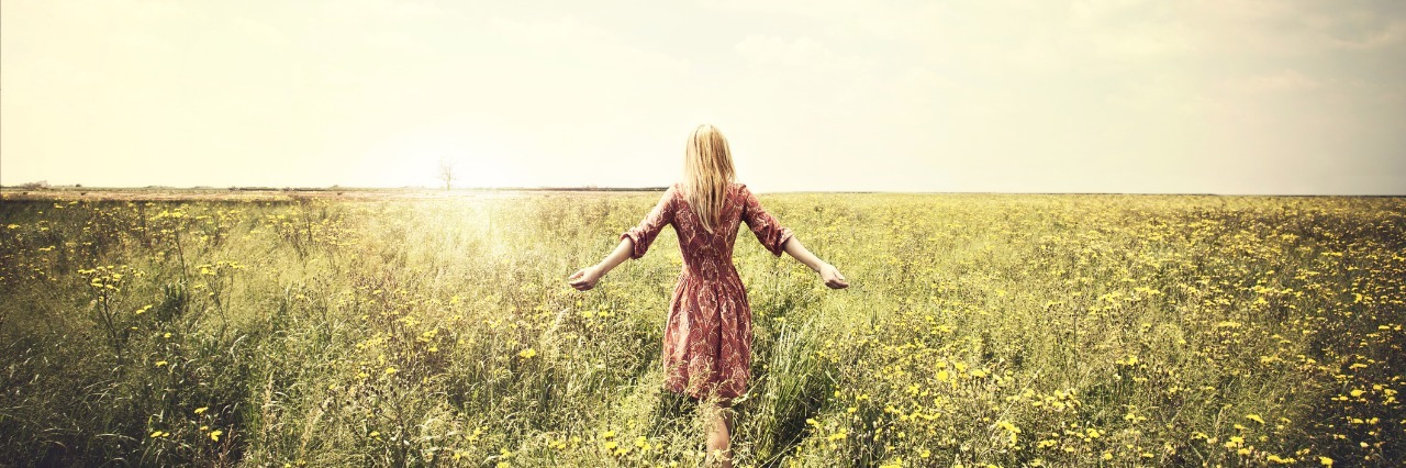 Feeling Thankful for Polycystic Ovary Syndrome woman in a red floral dress walking through a field toward the sun