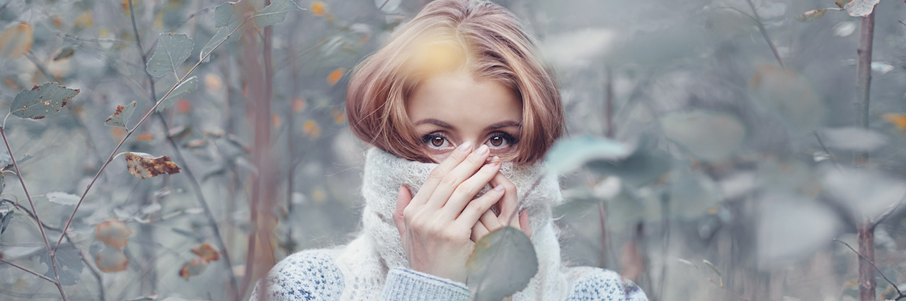 Eating Disorder Recovery: Why I'm Not Making a New Year's Resolution A woman standing outside covering her face with the neck of her sweater