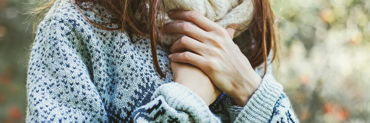 Self-Harm: Learning to Love Yourself woman wearing a sweater and a scarf clutching her hands in front of her chest