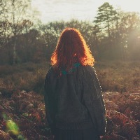young woman standing in forest at sunset