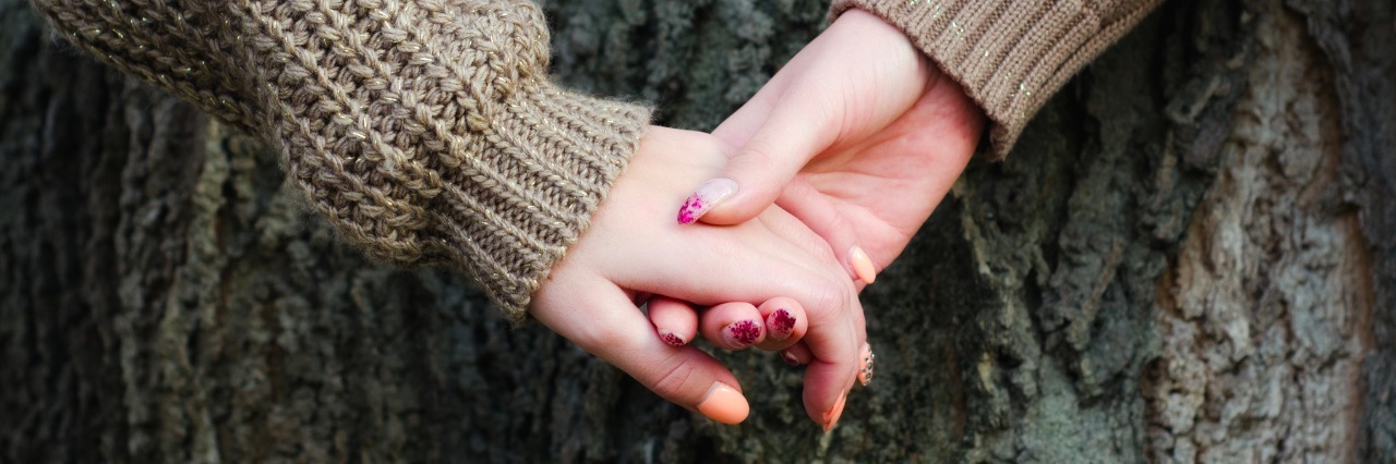 girls holding hands against tree bark in autumn