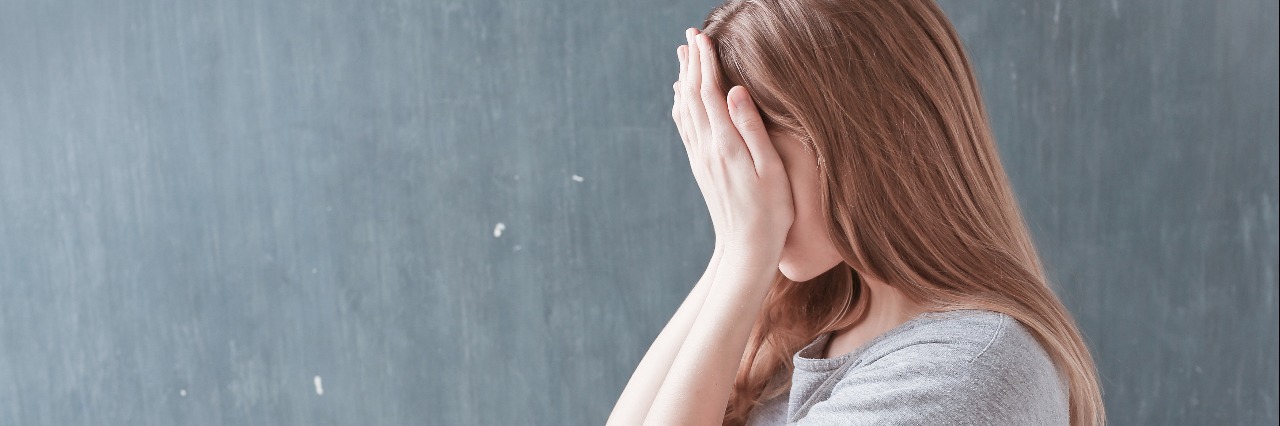 side view of woman in gray shirt holding her face in her hands