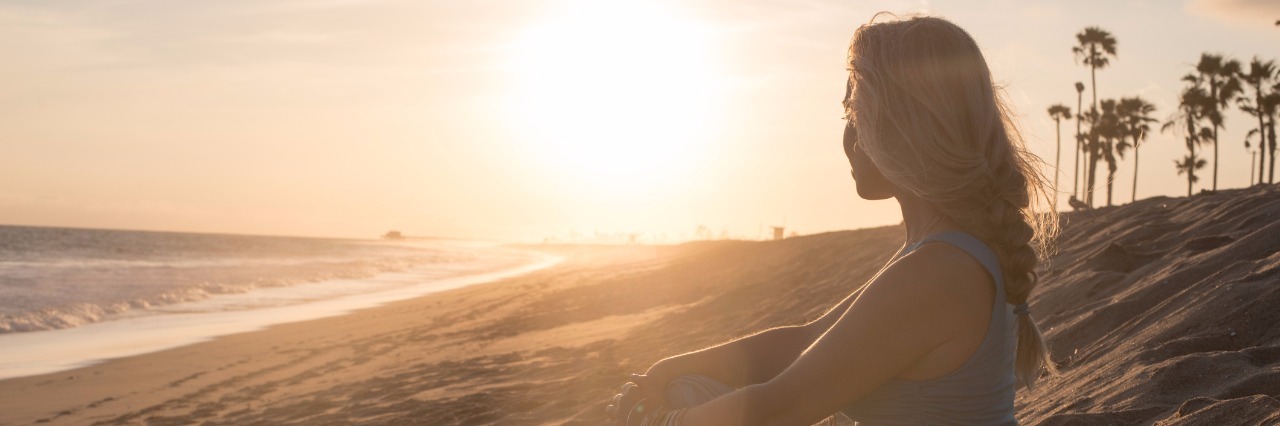 Adapting to a New Lifestyle With Illness young woman in a blue dress sitting on the beach and watching the sunset