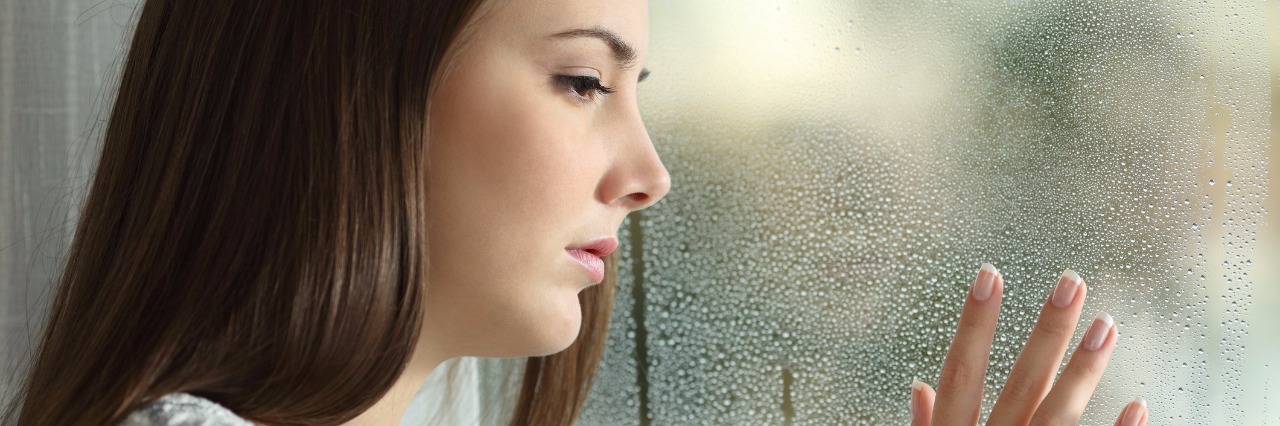 sad woman looking the rain falling through a window
