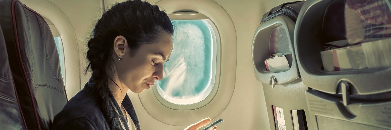 Woman sitting at airplane and looking at mobile phone.