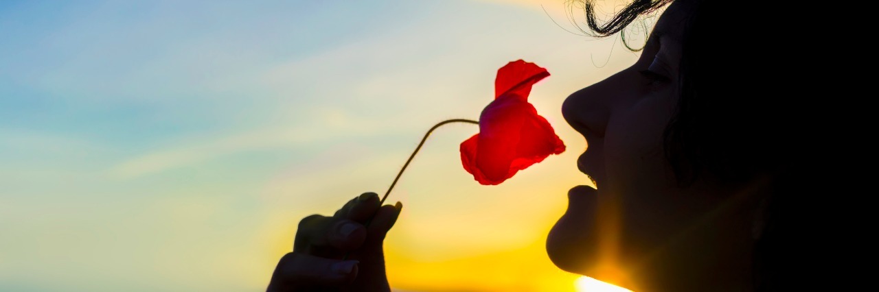 young woman smelling a poppy flower as the sun sets