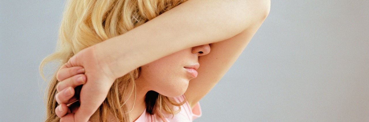 Reactions to Being Diagnosed With Endometriosis side view of a woman in a pink shirt covering her face with her arm